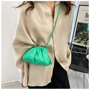 Detail of bright green pleated cloud pouch bag with slim strap on a beige satin shirt