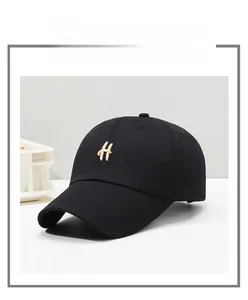 Detail of a black cotton baseball cap featuring a premium golden H-letter metal emblem