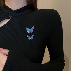 Detail view of two blue butterfly brooches with rhinestones on a black ribbed sweater