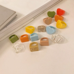 Gros plan de bagues en résine colorées en forme de cœur et carrées sur livre blanc