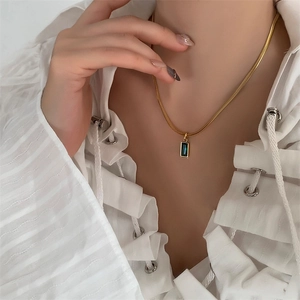 Detail of emerald green rectangular stone pendant on a gold snake chain necklace