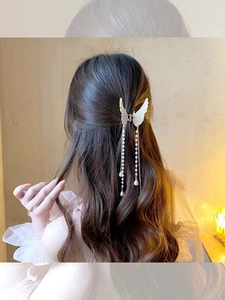 Detail of metal hair claw clip with angel wing design and hanging pearl tassels on hair