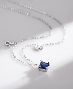 Makroaufnahme der S925 Silberkette mit blauem Edelstein und Logo-Anhänger im Detail