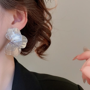 Gros plan d'un mannequin portant de grandes boucles d'oreilles fleurs argentées ciselées
