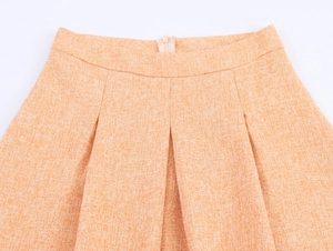 Détail d'une jupe plissée en tweed orange à taille haute avec fermeture éclair invisible