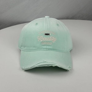Close-up of mint green baseball cap with embroidered letters and distressed brim