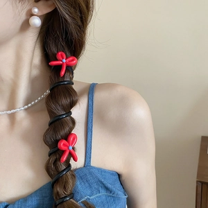 Détail d'un élastique spirale avec nœud rouge et perle bleue sur une queue de cheval tressée