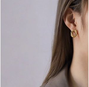 Gros plan d'une boucle d'oreille géométrique torsadée en or portée par un mannequin