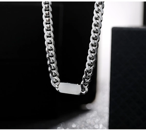 Detail of silver Cuban link necklace featuring a smooth rectangular pendant on dark texture