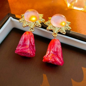 Macro view of vintage gold earrings with pink beads and red resin flower petal drops