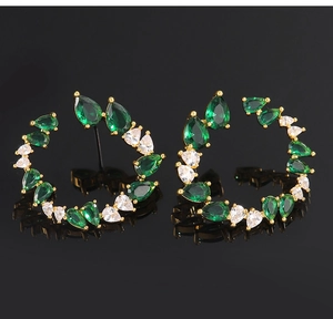 Detail of C-shaped gold hoop earrings featuring green and white teardrop zircon stones