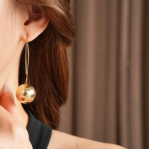 Mannequin portant de longues boucles d'oreilles dorées avec pendentif sphère mate