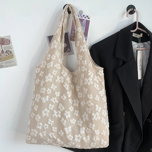 Detail of cream-white tote bag with 3D floral embroidery hung against a minimalist wall