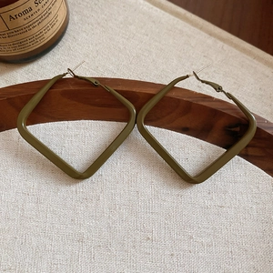 Close-up of matte dark green geometric square earrings on a minimalist wooden tray