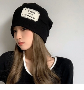 Detail of a black knit beanie featuring a white 'SEASON' patch and fine ribbed texture