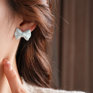 Close-up of light gray matte bow stud earrings worn by a model with soft lighting
