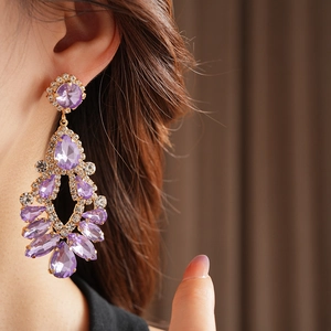 Detail shot of golden teardrop tassel earrings with purple crystals on a model