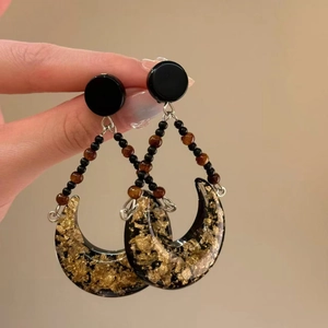Detail of crescent leopard earrings with gold foil accents and beaded fringe hangings