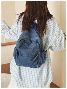 Detail of vintage blue denim backpack showing washed texture and woven straps on model
