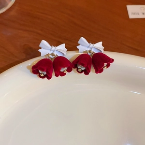 Detail of floral earrings with white frosted bows and dark red velvet lily buds on a ceramic dish