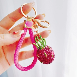 Detailed shot of a rhinestone dragon fruit keychain with pink braided cord and gold clip
