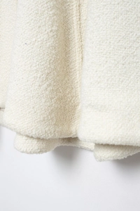 Macro close-up showing the soft textured cream-colored boucle fabric of the women's cloak