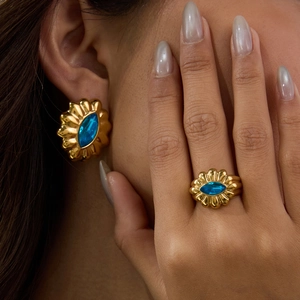 Close-up of gold flower ring and earring set featuring oval blue gemstones on a model