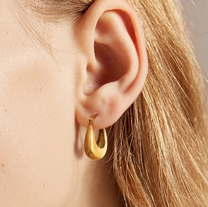 Macro shot of polished gold water drop earrings worn on ear showing glossy metallic finish