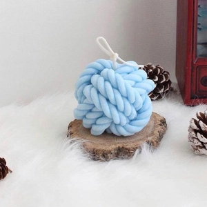 Blue knit yarn ball candle on rustic wood slice with a cozy winter atmosphere