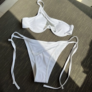 Detail of white two-piece bikini featuring mesh splicing and underwire cups on grey fabric