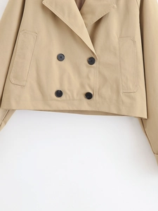 Detail of khaki cropped trench coat showing double-breasted black buttons and twill fabric