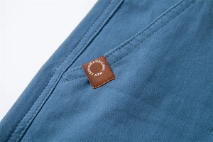 Macro view of blue cotton twill shorts with brown leather patch and double stitching