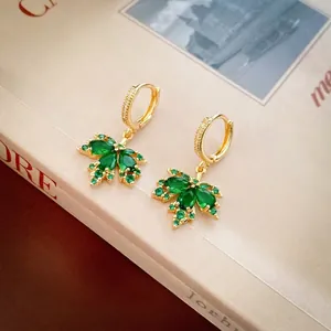Gold plated maple leaf huggie earrings with green zircon crystals on vintage book background