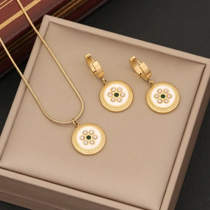 Macro detail of gold snake chain necklace and pearl earrings set with green stone