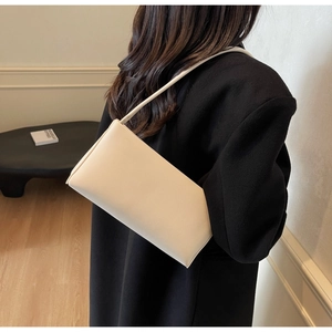 Close-up of a minimalist white leather baguette underarm bag worn on a black coat