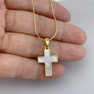 Golden cross necklace with white mother of pearl inlay held against a plain background