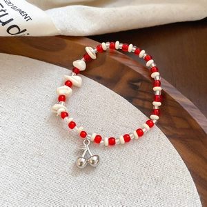 Detailed shot of beaded bracelet with red cherry pendant on a wooden tray