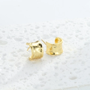 Macro detail of gold hoop earrings with irregular hammered texture on stone background