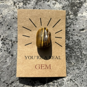 Macro shot of tiger eye stone on a kraft card with the text YOU'RE A REAL GEM
