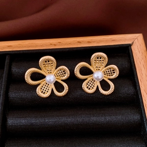 Close-up of golden hollow mesh flower earrings with central white pearl on black velvet