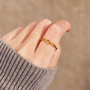 Elegant gold heart knot ring with central sparkling stone worn on female finger