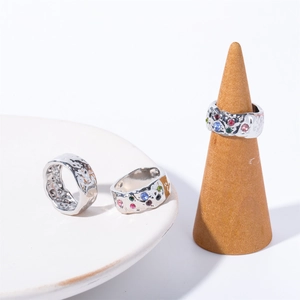 Detailed view of silver textured rings with colorful zircons on a white ceramic plate