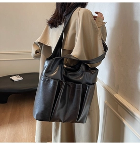 Detail view of a large black leather tote bag with multiple pockets worn by a model