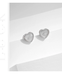 Dettaglio macro di orecchini a cuore in argento con trama perlata su base geometrica