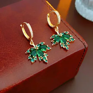 Gold plated maple leaf earrings with green zircon stones on luxury leather background