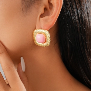 Close-up of vintage golden twisted square stud earrings with pink resin stone on model