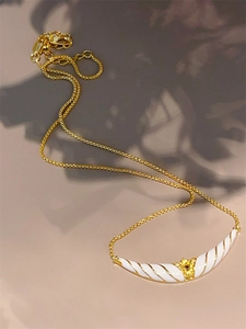 Vintage 18K gold necklace with white enamel horn pendant and soft leaf shadows