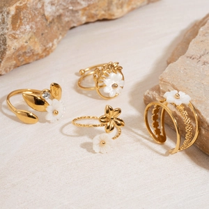 Detail of four gold rings featuring white shell flower designs and zircon accents