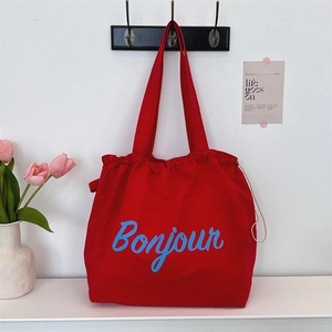 Detail of red canvas tote bag featuring blue Bonjour lettering and a drawstring closure