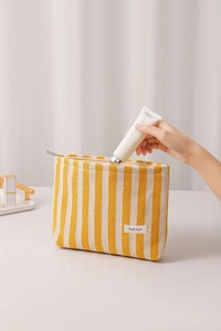 Detail of yellow striped canvas makeup bag with zipper closure and hand placing items